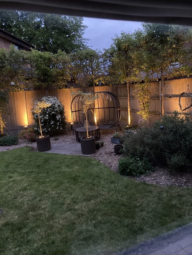 Beautifully maintained garden with painted fence and warm uplighting at dusk